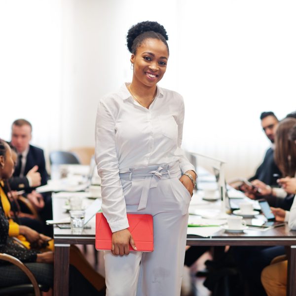 Face of handsome african american business woman, holding tablet on the background of business peoples multiracial team meeting, sitting in office table.